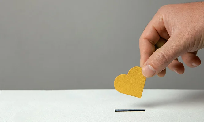 Man’s hand places heart in the donation slot. The concept of the donor of blood or human organs, saving lives. Copy space for text