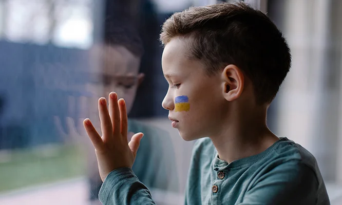 the child sits at the window with the flag of ukraine. State support in war. United Europe against Russia. Hope for the world. Anxiety and anticipation. Children's tears. Save Ukraine